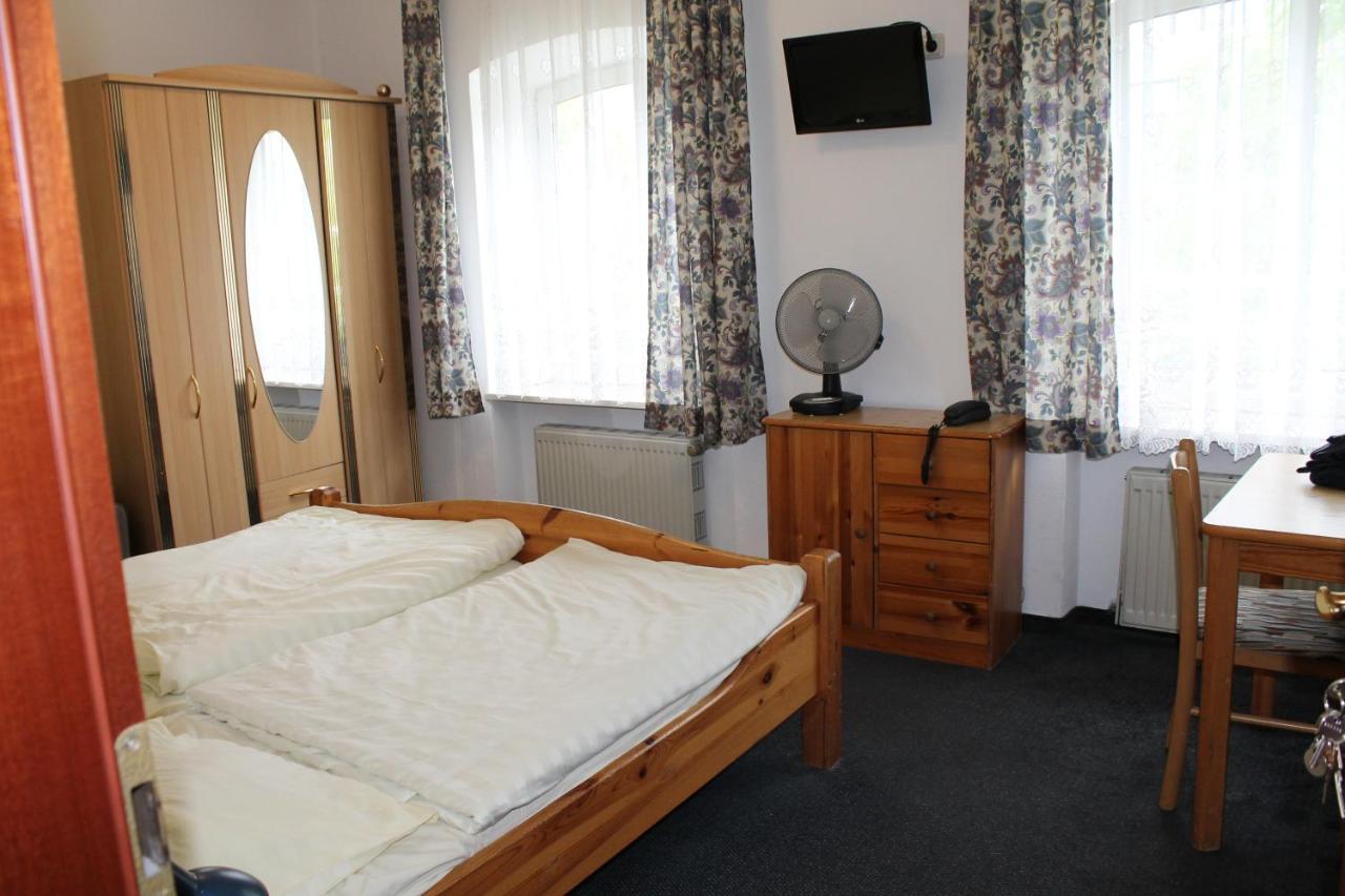 simple hotel room with wood bed frame, floral curtains, and small fan on a dresser